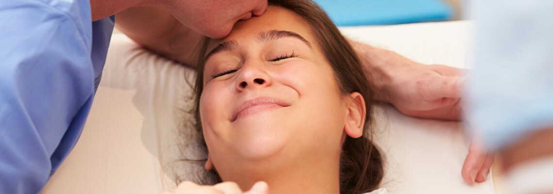 Mann küsst lächelnde Frau in Behandlungsraum auf die Stirn