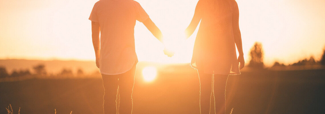 Paar läuft Hand in Hand bei Sonnenuntergang über eine Wiese