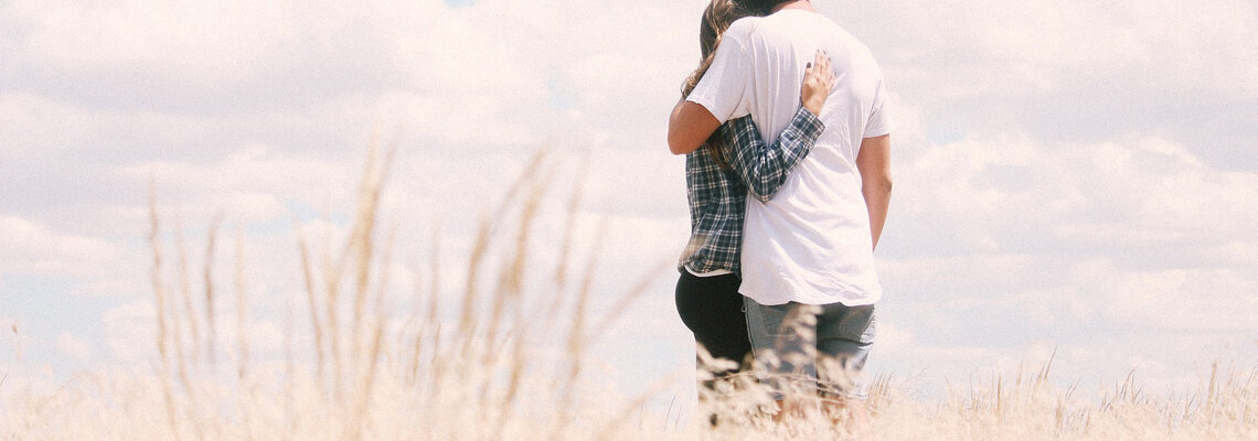 Ein Paar steht Arm in Arm in einem Feld und blickt in den Himmel