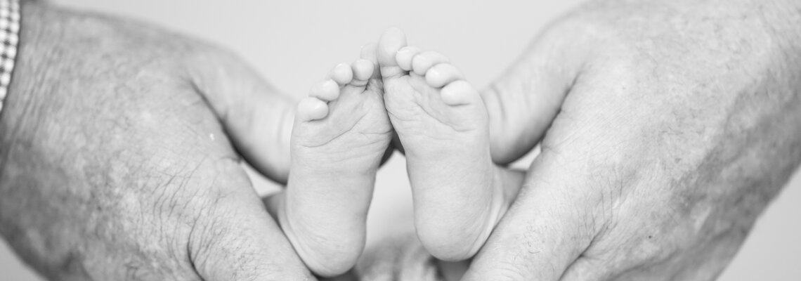 Schwarzweißbild von Männerhänden, die die kleinen Füße eines Neugeborenen umschließen