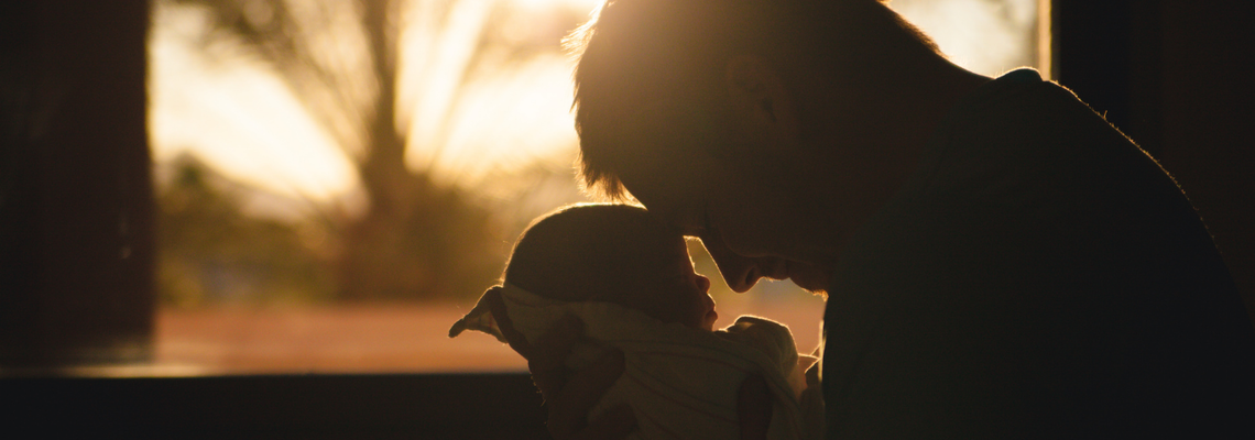 Vater Stirn an Stirn mit seinem Baby vor dem Fenster mit Sonnenuntergang