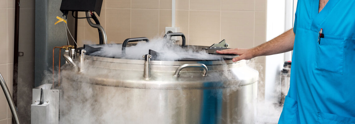 Embryologe steht neben Flüssigstickstofftank mit eingefrorenen Embryonen, Eizellen und Spermien